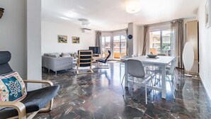 Ein geräumiger Wohnbereich mit Esstisch, modernen Stühlen, einer Couch und einem Fernseher.