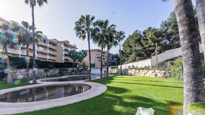 Eine angelegte Grünfläche mit Pool, Palmen und einem Gebäude im Hintergrund.