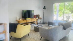 Ein Wohnzimmer mit einem Flachbildfernseher, einer Holzunterhaltungsecke, einem gelben Sessel, einem grauen Sofa und einem großen Fenster.
