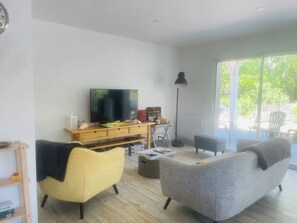 Ett vardagsrum med en platt-TV, en möbel i trä för underhållningsutrustning, en gul fåtölj, en grå soffa och ett stort fönster.