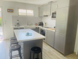 Ett modernt kök med en central köksö, barstolar, en mikrovågsugn och en diskmaskin.