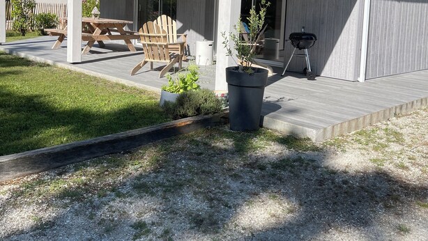 Ein überdachter Patio-Bereich mit Holztisch und Stühlen, einem Grill und einem Blumentopf.
