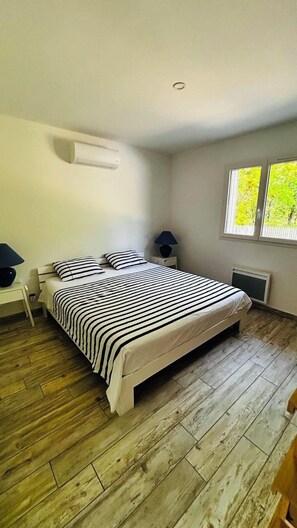 A bedroom with a bed, bedside tables, a lamp, a window, and a wall-mounted air conditioner.