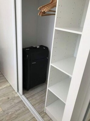 A closet with a black suitcase and a white shelving unit.