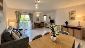 A spacious living area with a sofa, dining table, and chairs, a TV, and a balcony with curtains. - ALBUFEIRA BALAIA GOLF VILAGE 1 WITH POOL by HOMING (Albufeira)
