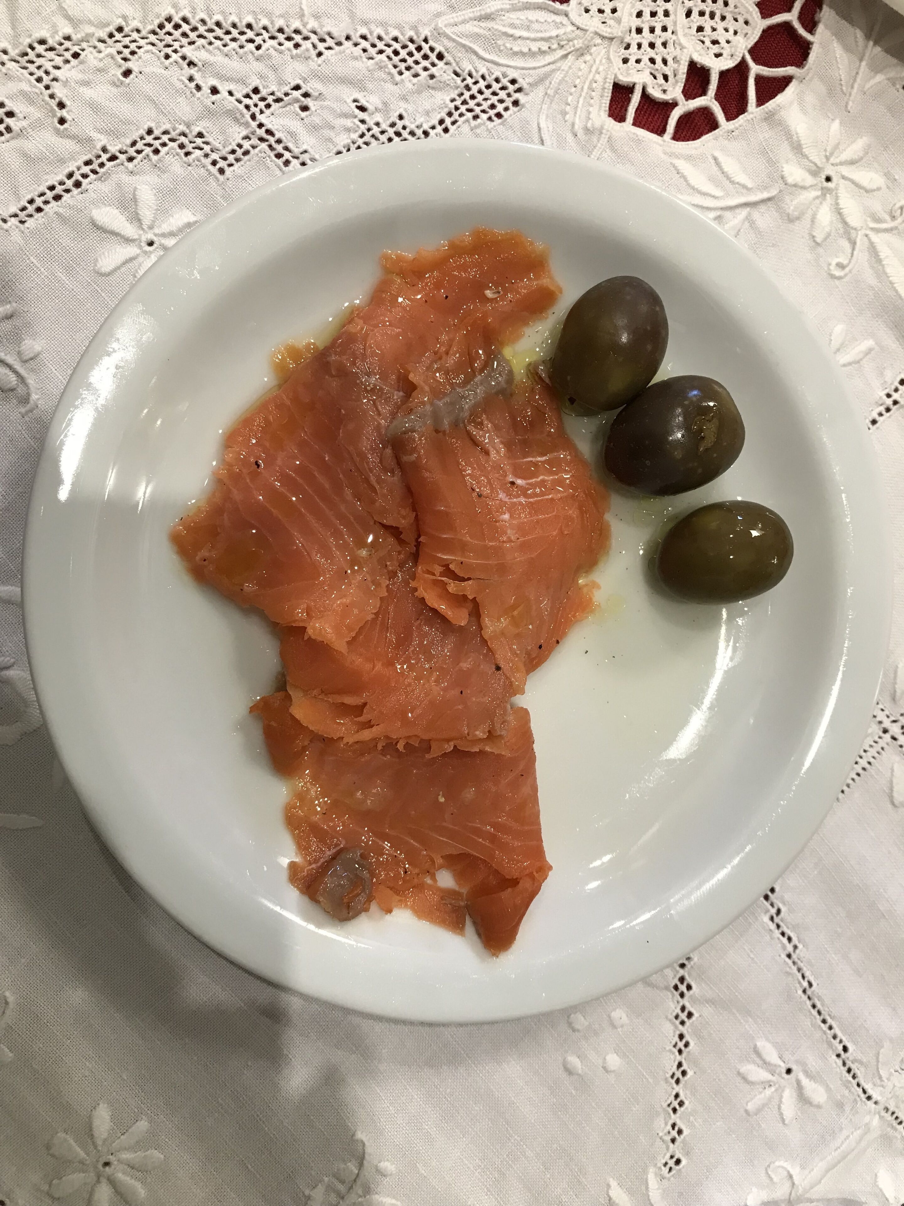 A plate with slices of salmon and olives on a white plate.