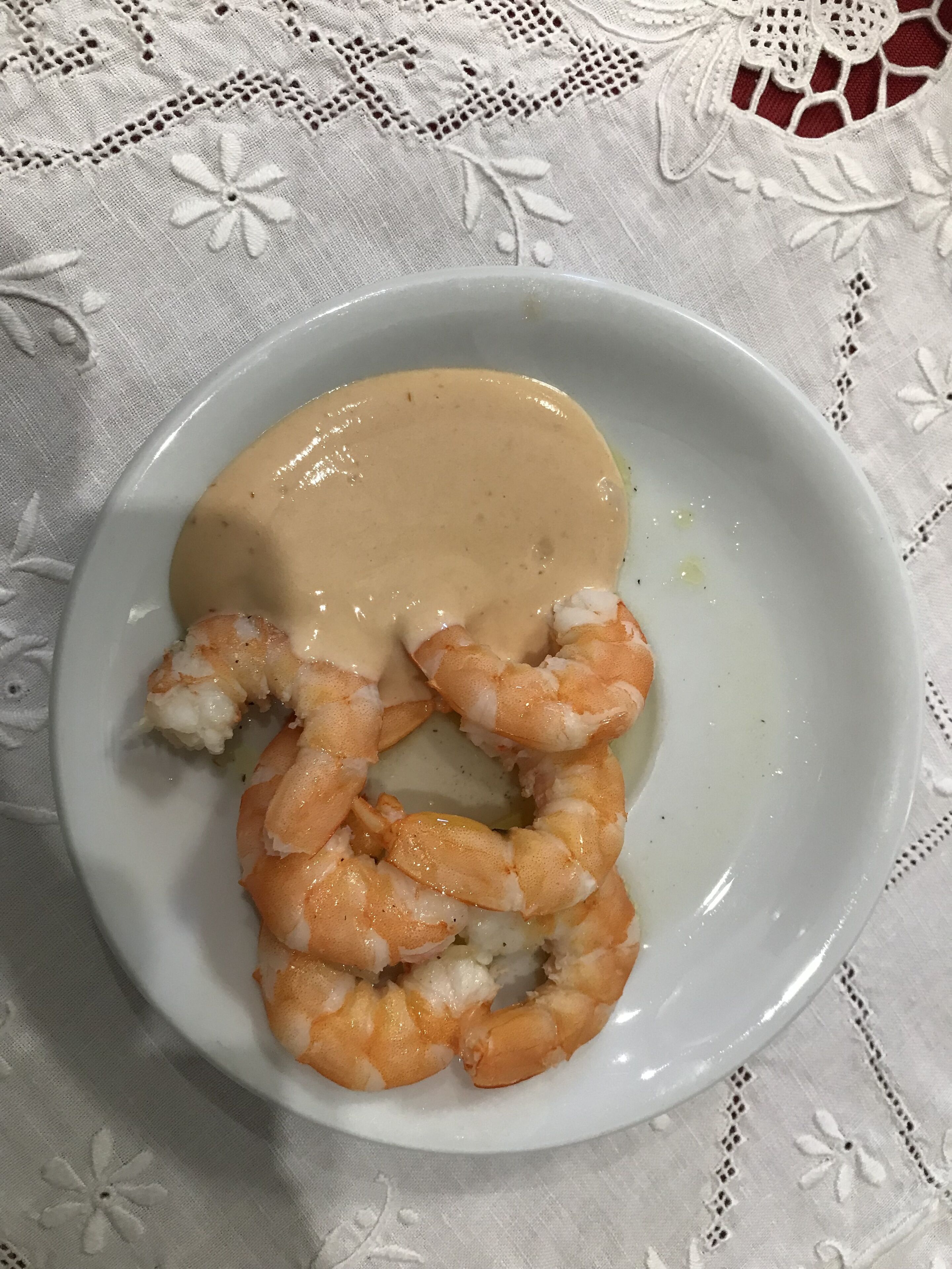 Une assiette de crevettes nappées d’une sauce crémeuse, le tout posé sur une nappe blanche.