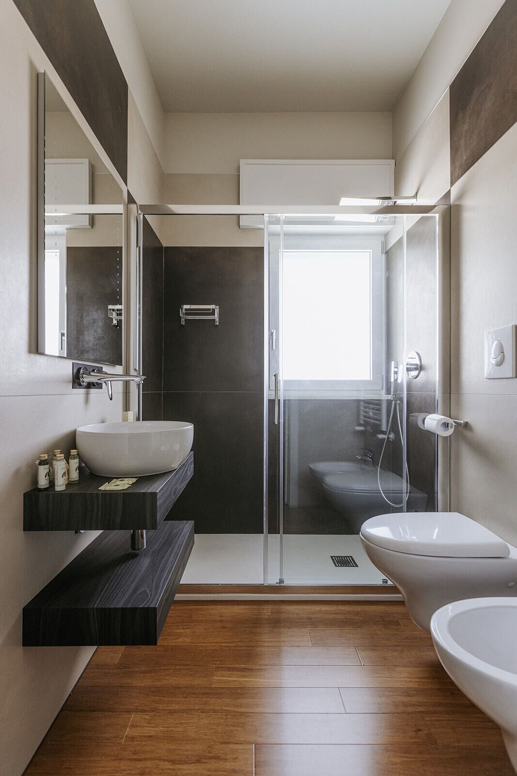 Une salle de bain moderne avec un grand miroir, un lavabo sur colonne, des toilettes et une douche à parois de verre.