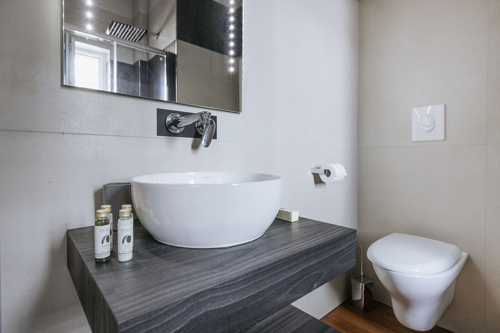 A bathroom with a white sink, a mirror, a toilet, and a vanity with toiletries.
