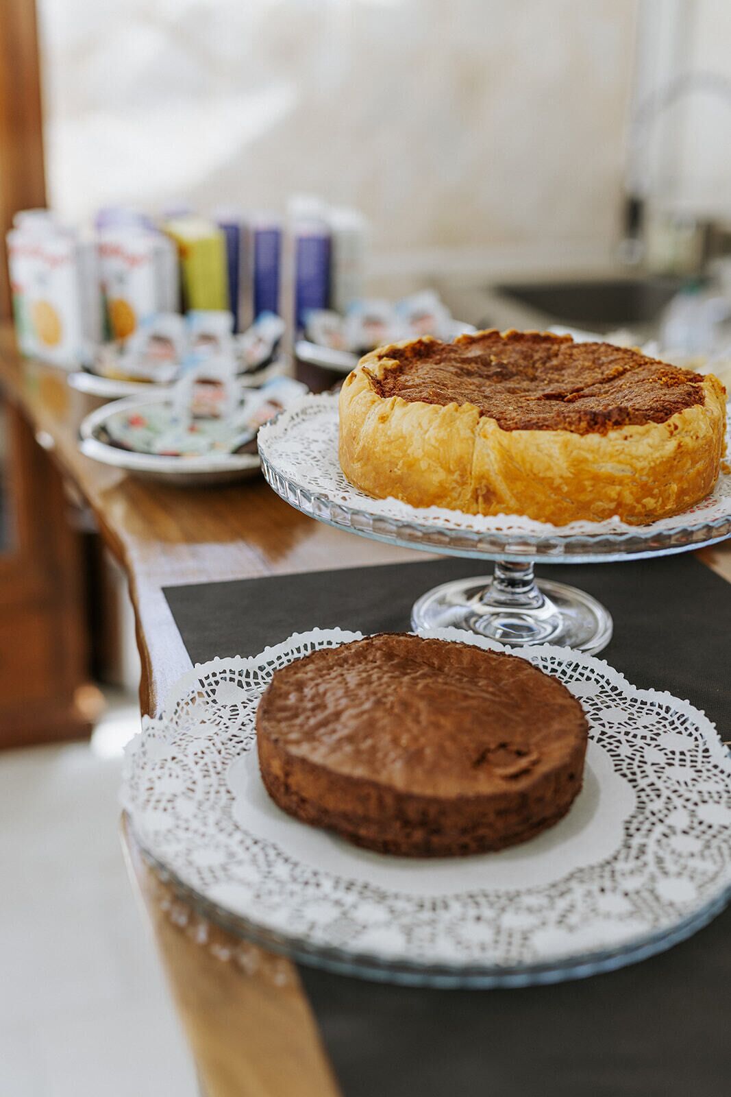 A table with two cakes on decorative stands, a lace doily, and a patterned plate.