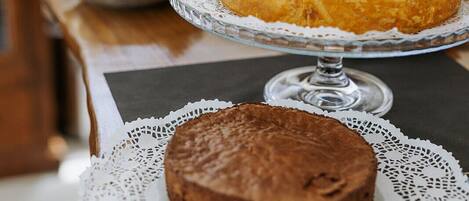Una mesa con dos pasteles sobre pedestales decorativos, un mantel de encaje y un plato estampado.