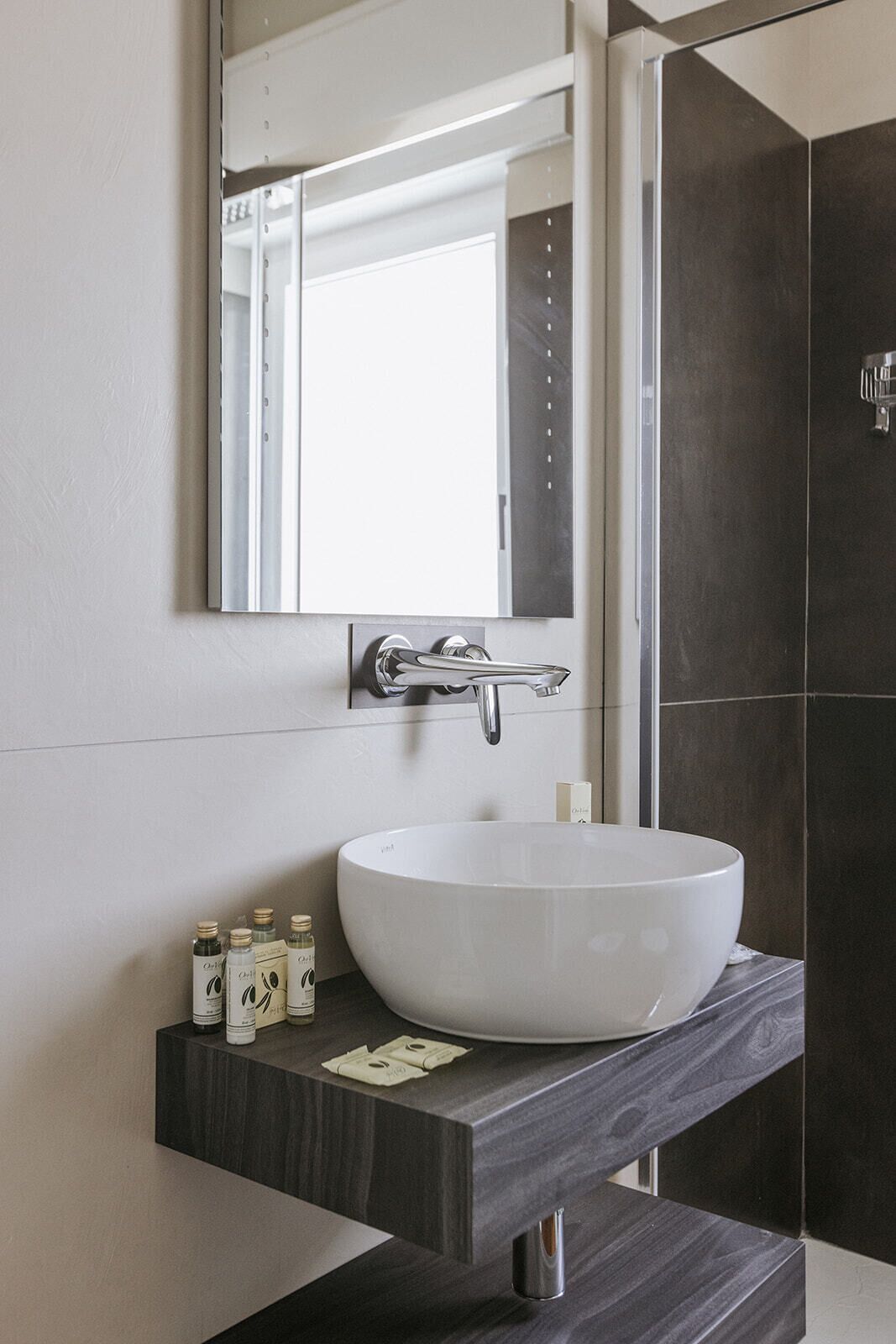 A modern bathroom with a white vessel sink, dark wood vanity, and a large mirror above the sink.