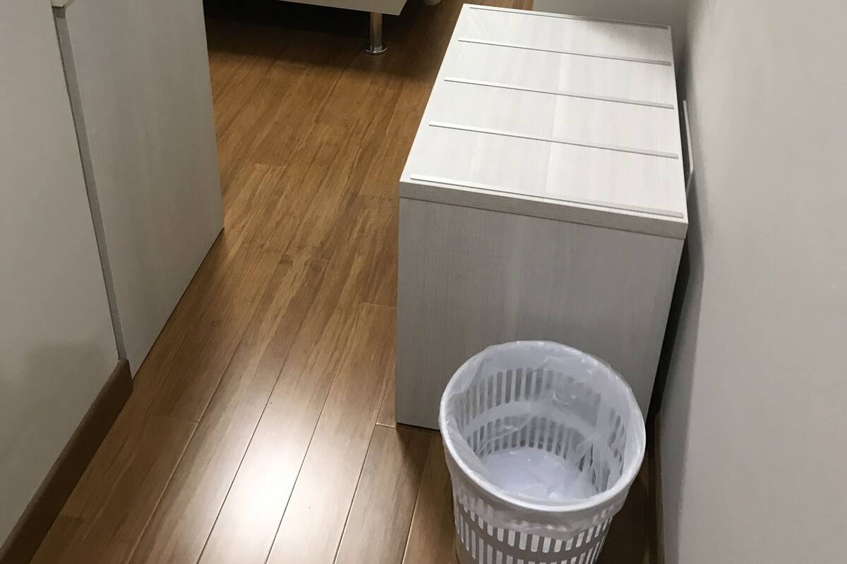 Ett litet, kompakt rum med en säng, ett litet skrivbord och en tvättkorg.