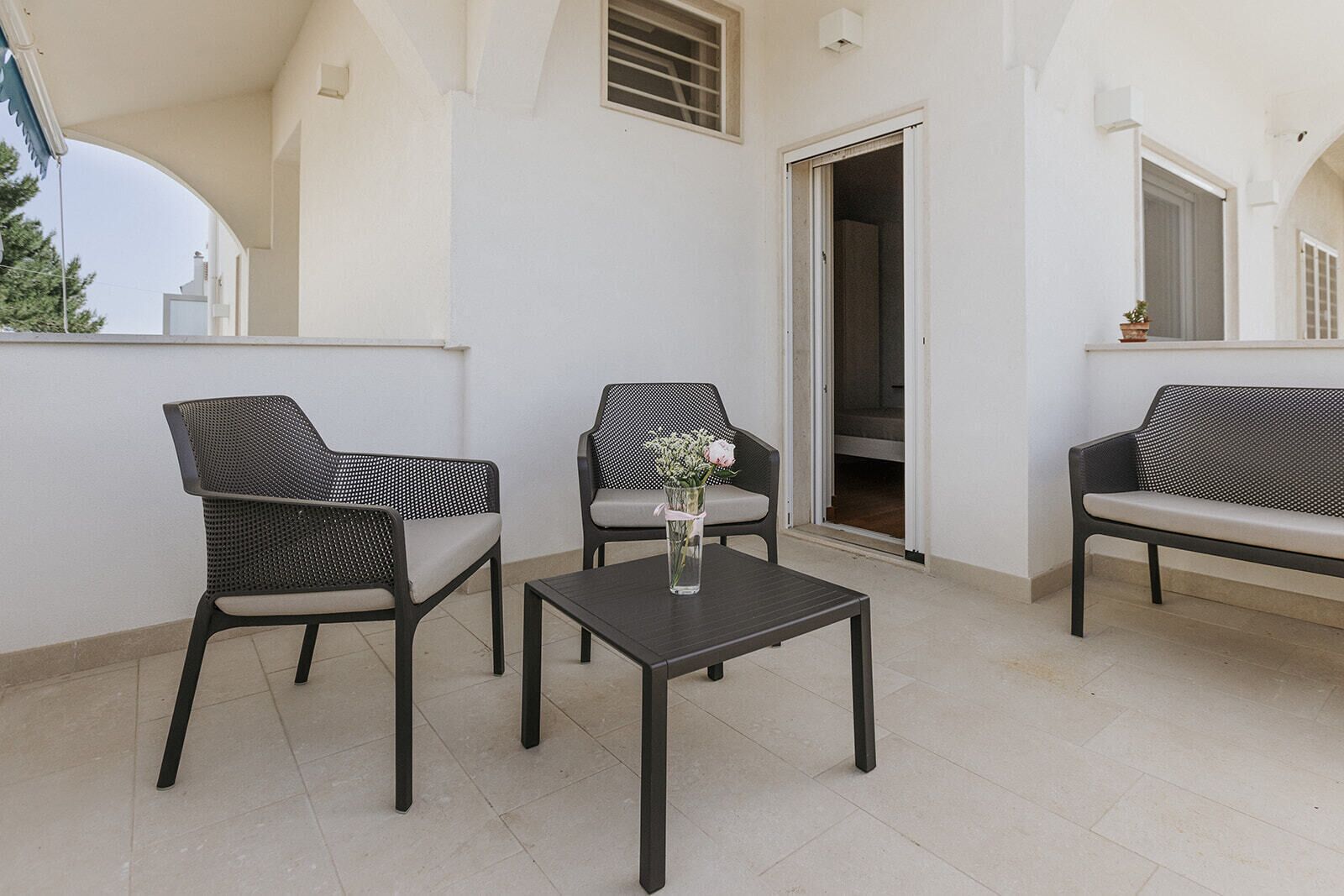Een balkon met twee stoelen, een tafel en een vaas met bloemen.