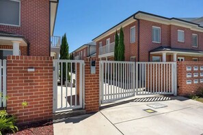 A residential building with brick exterior, white gates, and a gated driveway.