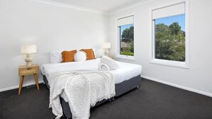 A bedroom with a bed, two bedside tables, a window, and a view of greenery outside. - Contemporary Living in the CBD (Wagga Wagga)
