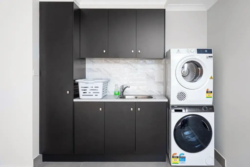 A compact kitchen with dark cabinets, a washing machine, and a drying machine.