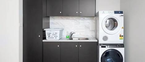 A compact kitchen with dark cabinets, a washing machine, and a drying machine.