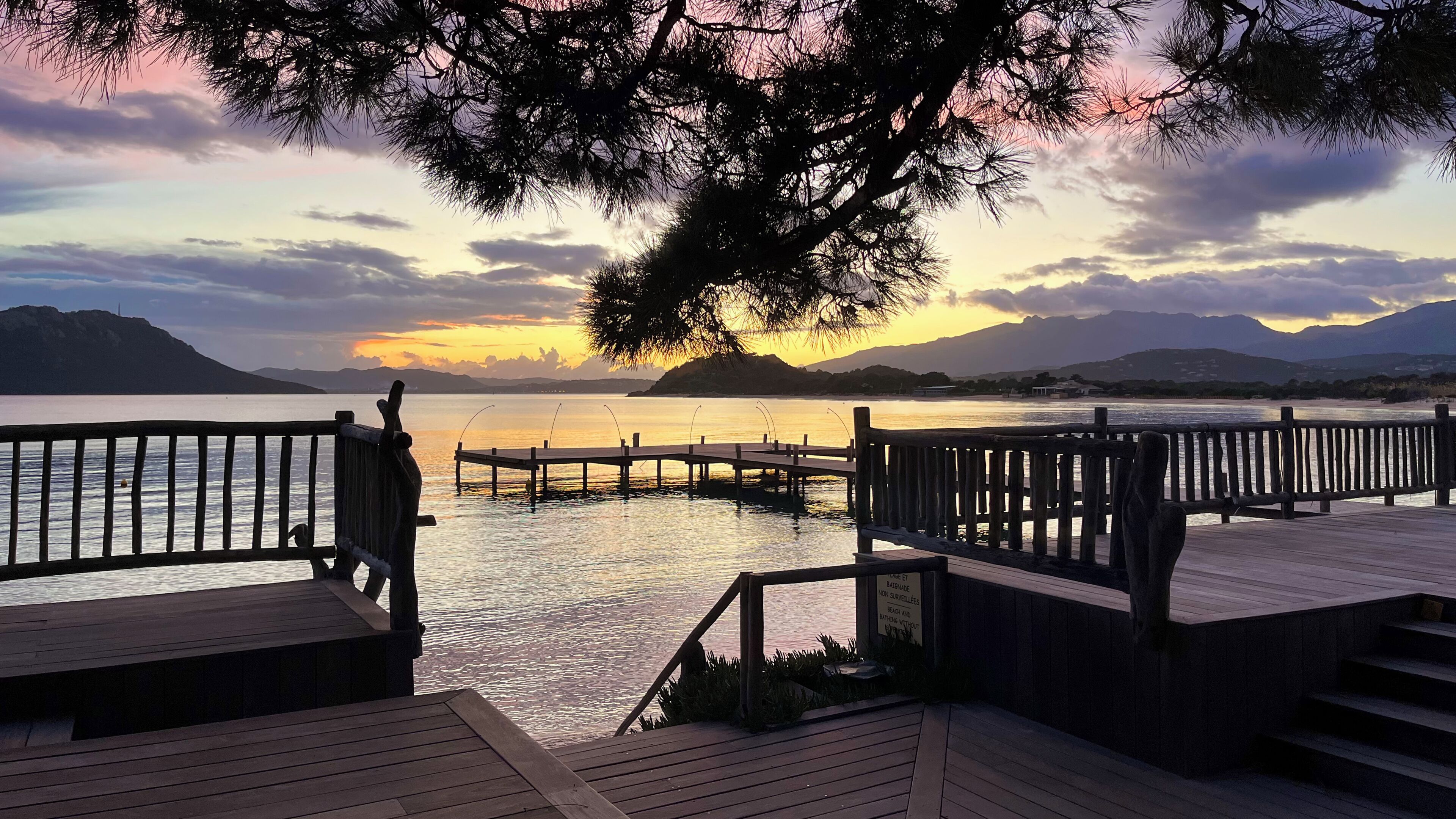 A wooden pier extending into calm water with a sunset in the background.