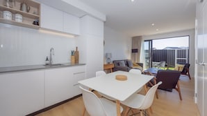 Uma cozinha moderna com armários brancos, uma mesa de jantar com cadeiras e uma sala de estar com sofá e mesa de centro.