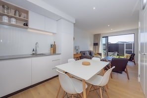 A modern kitchen with white cabinetry, a dining table with chairs, and a living area with a sofa and a coffee table.