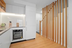 A modern kitchen with white cabinets, a built-in oven, and a wooden staircase.