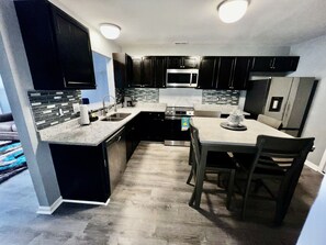 Een moderne keuken met donkere kastjes, een centraal eiland en een eethoek met stoelen.