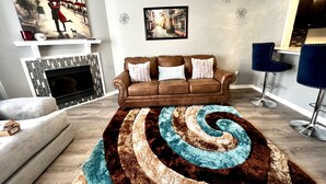 A living room with a brown sofa, a patterned rug, a fireplace, and two bar stools. - 2bd 2.5 ba Sleeps 6 Luxury Townhome, Jacksonville NC. Close To Camp Lejeune (Jacksonville)