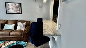 A modern living room with a brown leather sofa, a blue chair, a patterned rug, and a kitchen area with a marble countertop. - 2bd 2.5 ba Sleeps 6 Luxury Townhome, Jacksonville NC. Close To Camp Lejeune (Jacksonville)