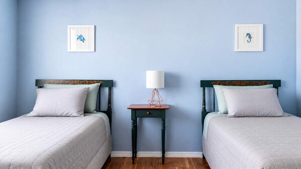 A room with two beds, a nightstand, and a wall with two framed pictures.