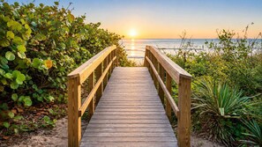 A wooden boardwalk leading to a beach with dense foliage on both sides. - Charming Beachside Escape Patio Parking (Indialantic)
