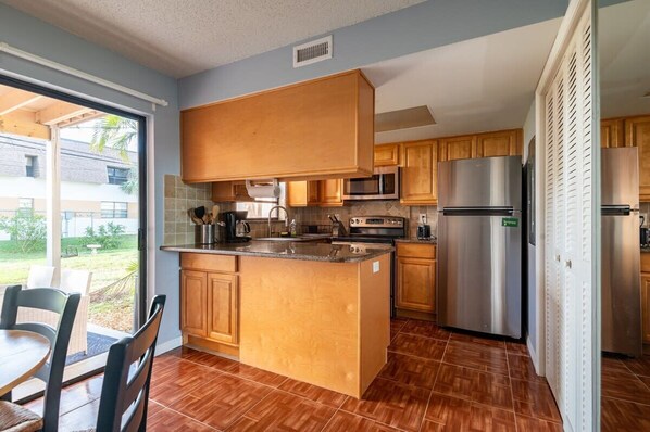 A kitchen with wooden cabinets, stainless steel appliances, and a large island. - Charming Beachside Escape Patio Parking (Indialantic)