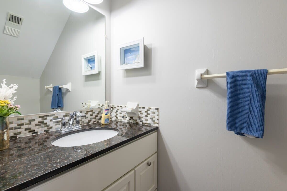 A bathroom with a white sink, a mirror, a towel rack with a blue towel, and a framed picture on the wall.