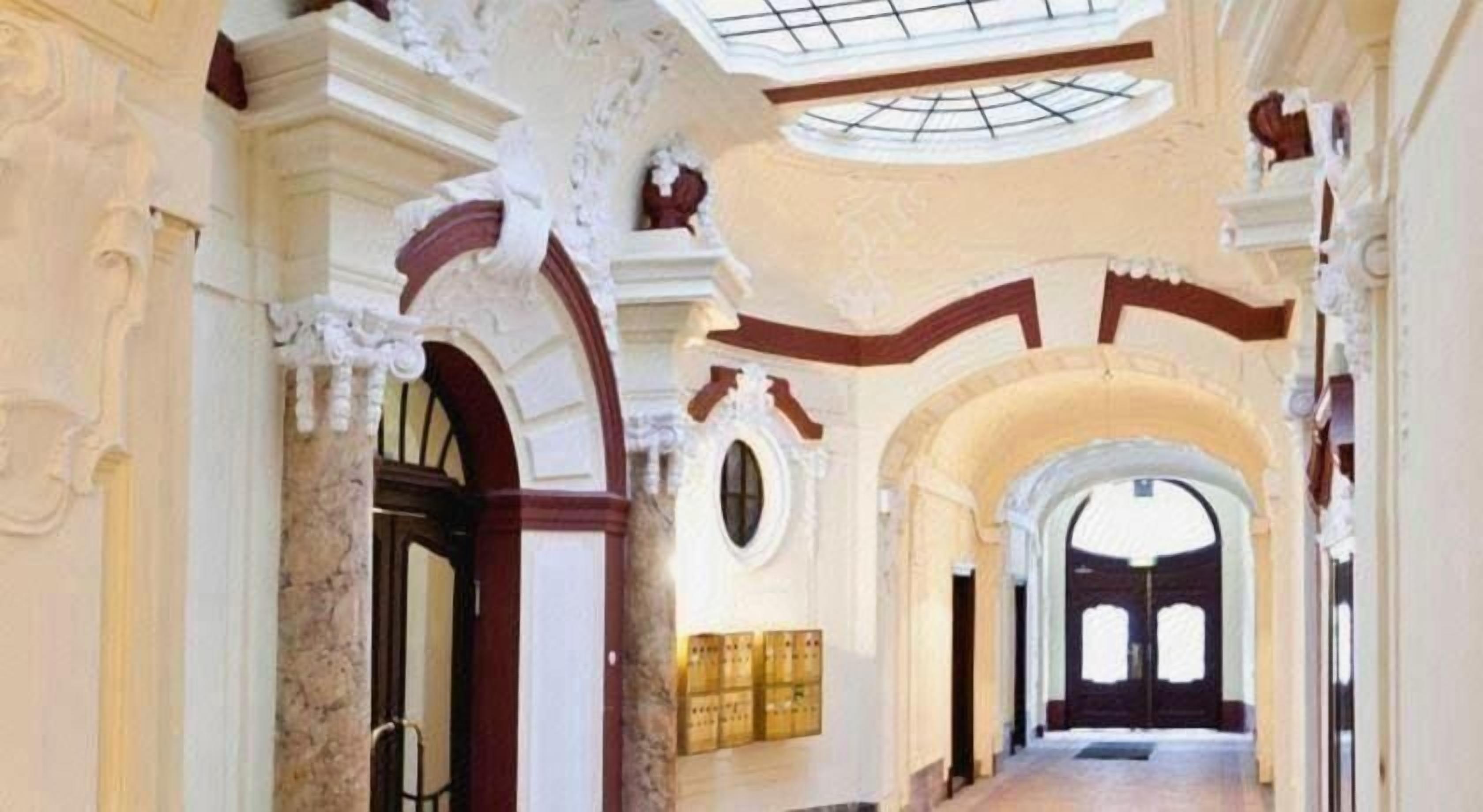 An interior with arched doorways, a skylight, and a long corridor leading to a darkened area.