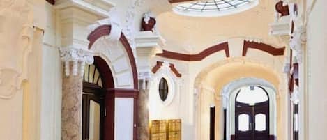 An interior with arched doorways, a skylight, and a long corridor leading to a darkened area.