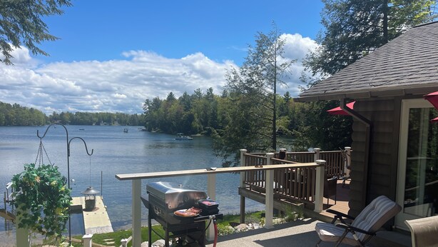 A lakeside patio with a grill, outdoor furniture, and a view of the lake. - Beautiful waterfront home on Mickey Lake, channeling to 2800 acre Long Lake. AC  (Traverse City)