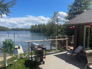 A lakeside patio with a grill, outdoor furniture, and a view of the lake.