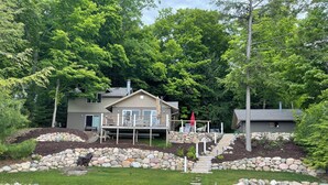 A lakeside cabin with a deck, stone steps, and a dock leading to a pond. - Beautiful waterfront home on Mickey Lake, channeling to 2800 acre Long Lake. AC  (Traverse City)