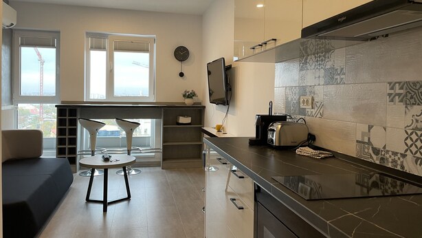 Uma cozinha moderna com uma ilha grande, um espaço de refeições com mesa redonda e vista para a cidade através de amplas janelas.