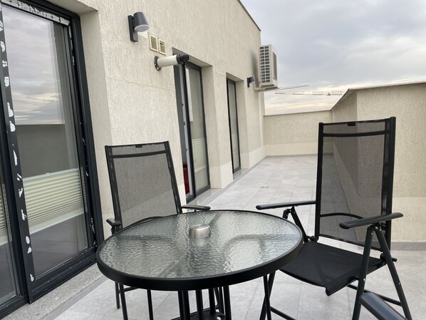 A glass-top table with two chairs, a window with blinds, and an air conditioning unit on a balcony. - 4 Room Penthouse Terrace W18-W19 (Bucharest)