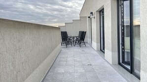 Terraço no telhado com mesa e cadeiras, uma grande porta de vidro deslizante e vista do céu.