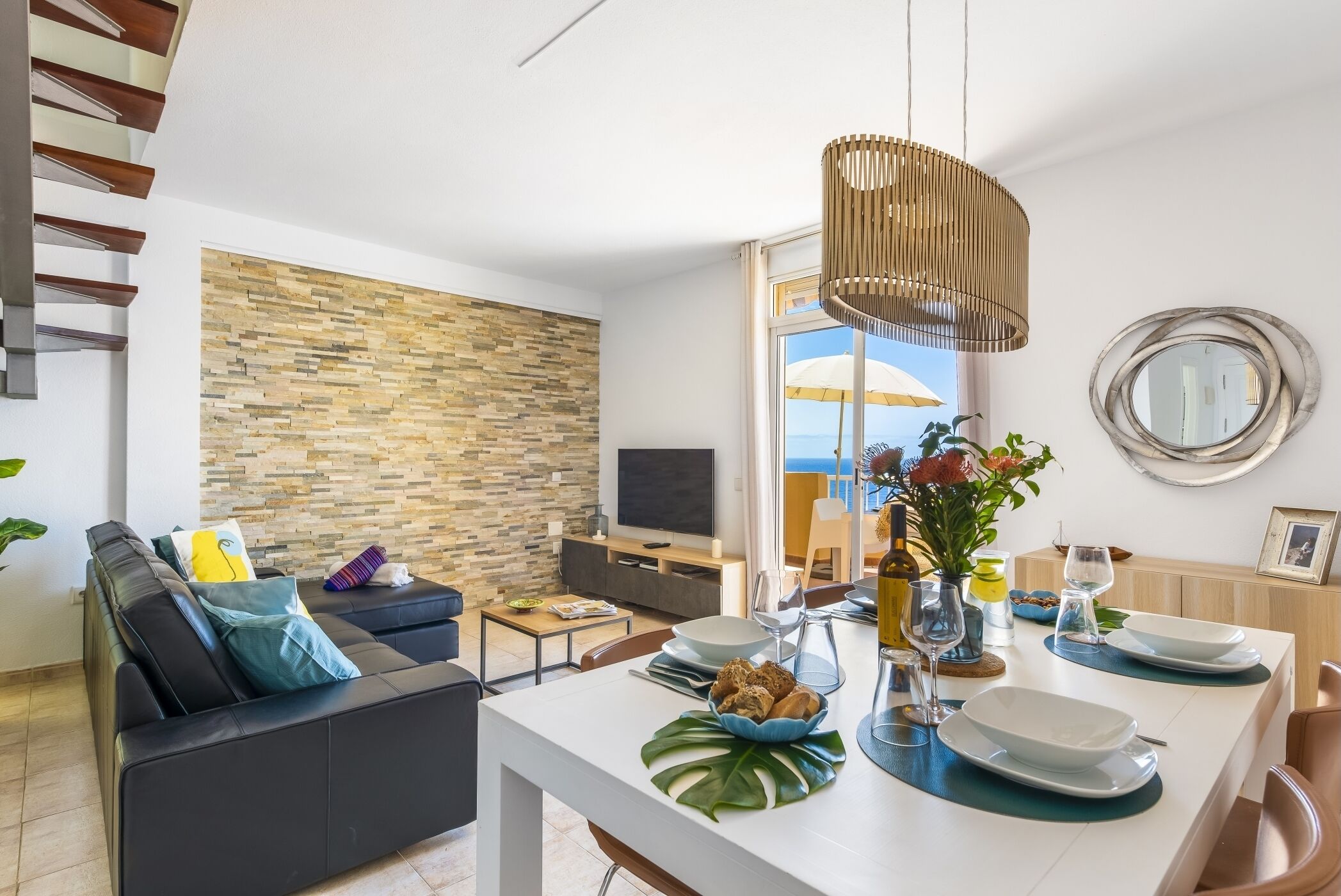 Un salon moderne avec un canapé, une table à manger dressée avec des assiettes et des verres, un téléviseur et un mur en pierre.
