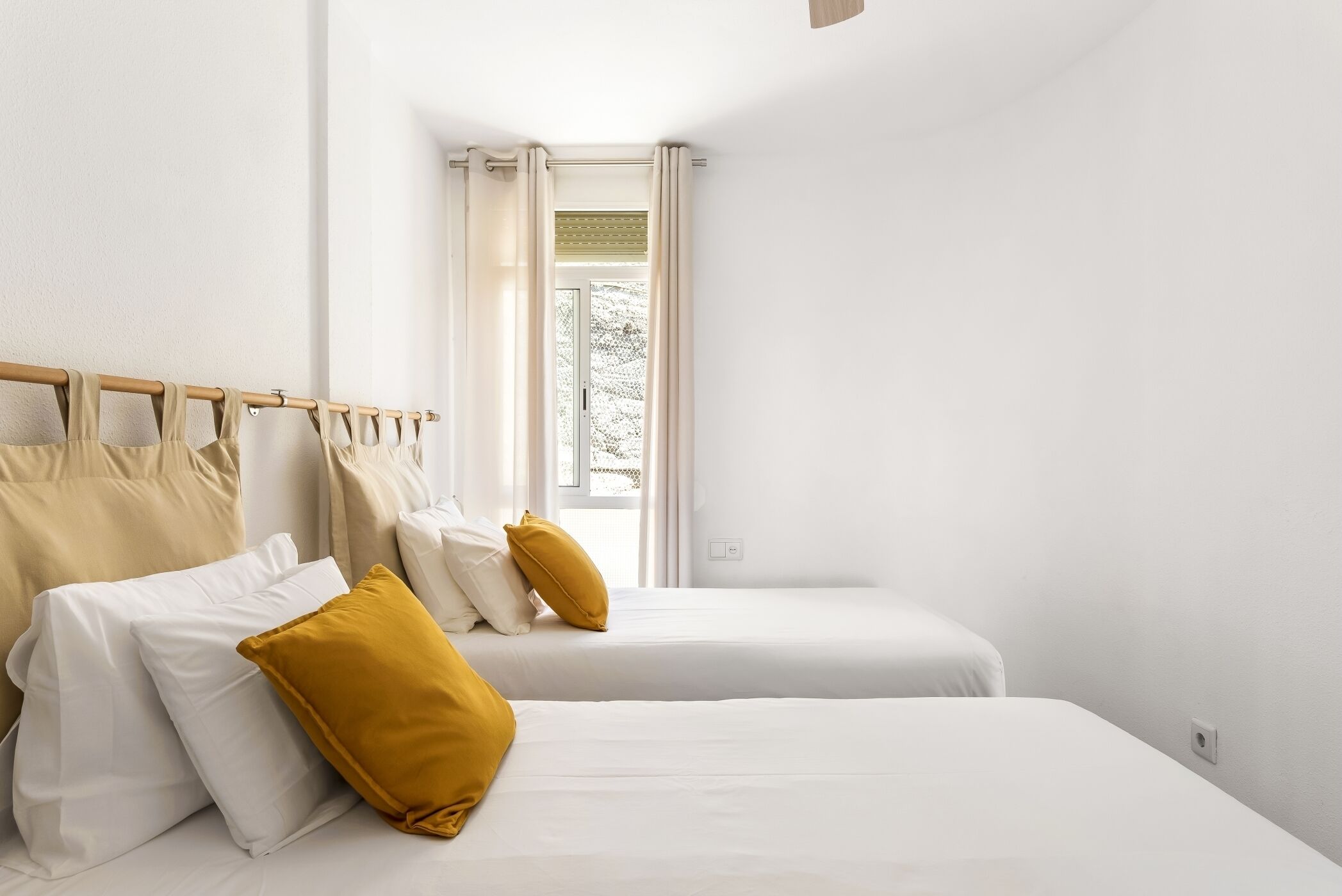 Een kamer met twee bedden, witte lakens en een raam met gordijnen.