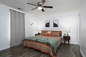 Quarto com cama, duas mesas de cabeceira, um ventilador de teto e dois quadros pendurados na parede.