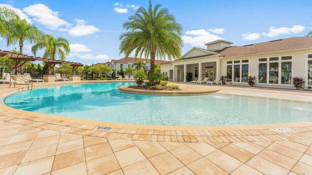 Une piscine avec un palmier au centre, entourée d’une terrasse carrelée et d’un bâtiment doté de grandes fenêtres.