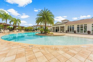 Une piscine avec un palmier au centre, entourée d’une terrasse carrelée et d’un bâtiment doté de grandes fenêtres.