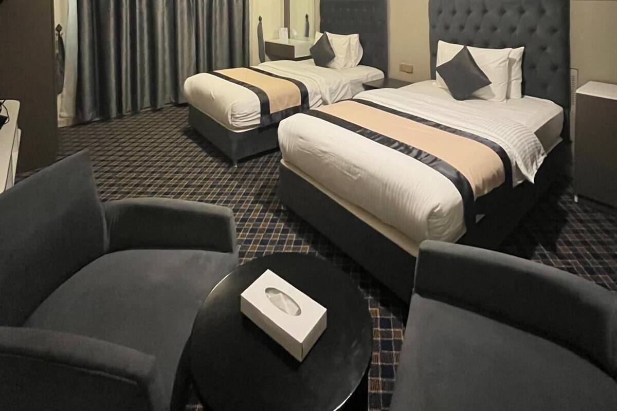 Habitación de hotel con dos camas, un escritorio, una silla y una mesa redonda con una caja encima.