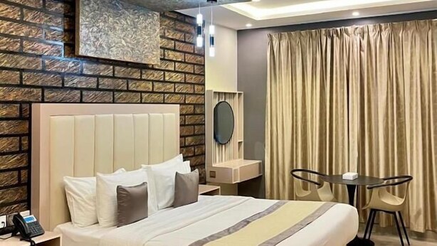 Una habitación de hotel moderna con una cama grande, una pequeña mesa con sillas, un teléfono en la mesita de noche y una pared con diseño de ladrillo.