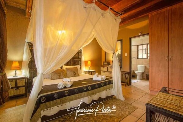 A bedroom with a four-poster bed, a wooden wardrobe, and a bathroom visible through an open door. - Villa - Sleeps 10 - Pool - Patio - Housekeeping (Nkomazi)