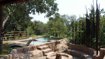 Relax by the serene pool surrounded by lush greenery and a natural rock formation.